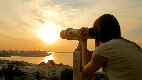 年轻女子透过旅游望远镜在夕阳下探索城市