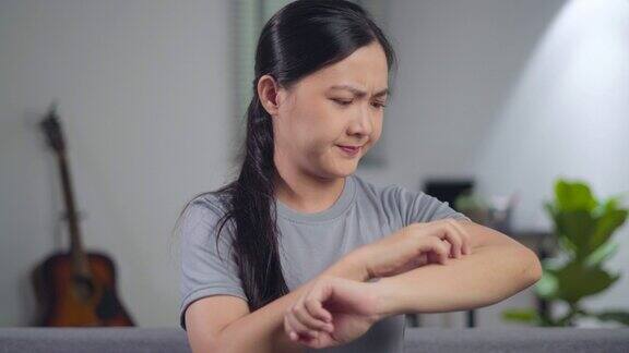 亚洲妇女生病了刺激瘙痒她的皮肤坐在客厅的沙发在家里