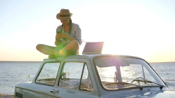 阳光下的汽车照片女孩坐在车顶复古车的背光在手机上自拍