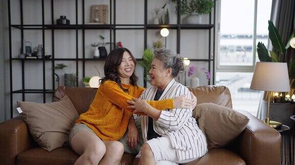 亚洲成熟的母亲和年轻的女儿拥抱在沙发客厅在家里