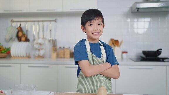 亚洲可爱小男孩的肖像系着围裙双臂交叉站在家里的厨房里对着镜头微笑烹饪与职业理念