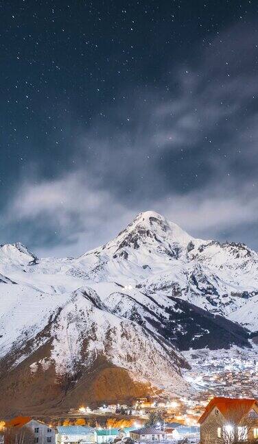 Stepantsminda格鲁吉亚冬夜星空与发光的星星和卡兹贝克山顶覆盖着雪美丽的夜晚格鲁吉亚冬季景观垂直镜头