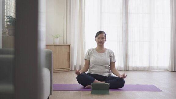 女人在家客厅练习瑜伽在平板电脑上观看在线教程