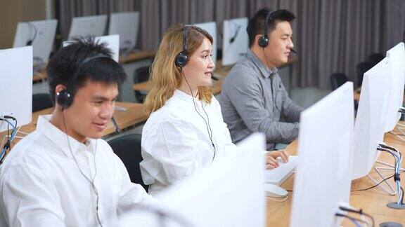 亚洲呼叫中心团队客户服务电话销售戴耳机或耳机与客户在现代办公室交谈