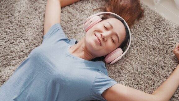 年轻的亚洲大学女子与休闲戴耳机躺在地毯地板上听音乐冷静放松在家里的客厅休息