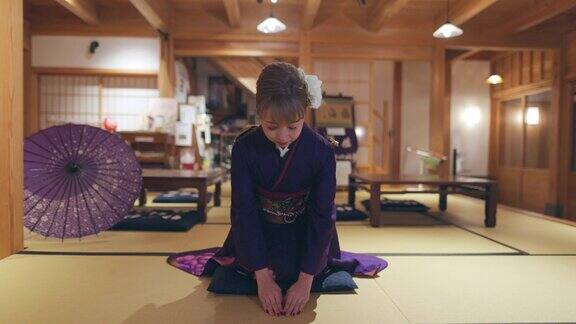 穿着Furisode和服的年轻女子坐在高跟鞋上在日本的榻榻米房间鞠躬