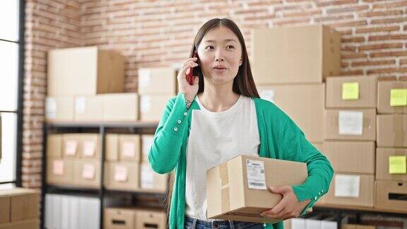 年轻的中国电子商务女员工在办公室拿着包裹谈论智能手机