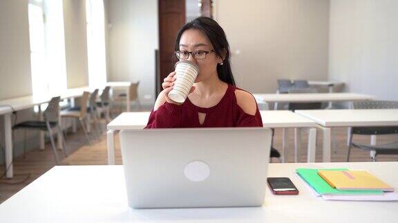 专注的亚洲女孩戴着眼镜坐在图书馆的桌子旁在笔记本电脑上学习