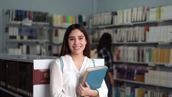 快乐的女学生站在图书馆对着镜头微笑