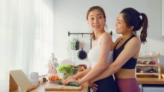 两个穿着运动服的亚洲年轻女子在厨房里做沙拉活泼漂亮的女孩姐姐感到快乐喜欢吃蔬菜健康的食物来减肥在家里的保健