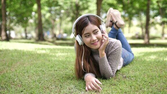 一个年轻的女孩躺在草地上戴着耳机享受喜爱的音乐
