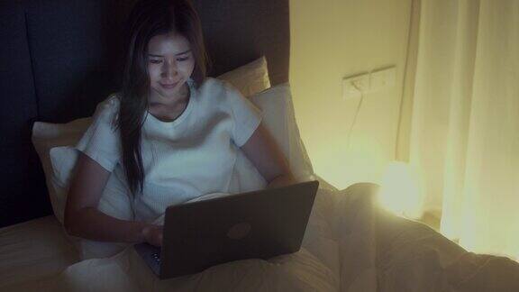 商务女性晚上在卧室坐在床上使用笔记本电脑