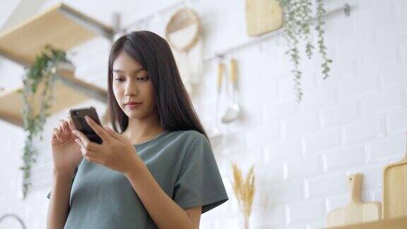 快乐的年轻亚洲女人在家里放松亚洲女性站在厨房柜台使用手机