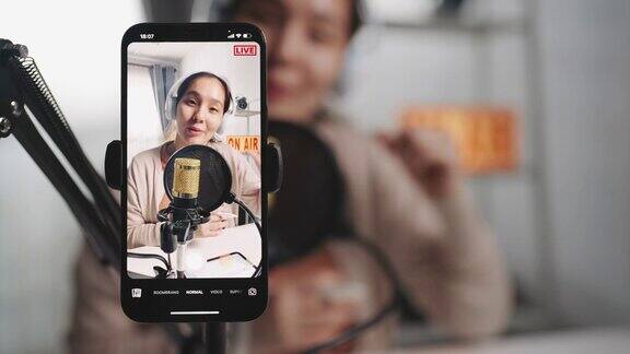 亚洲女性网红使用麦克风戴耳机用智能手机录制内容用于在线社交媒体