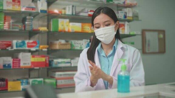 亚洲女性药剂师戴着医用外科口罩使用酒精凝胶在现代药店的肖像covid-19和大流行概念