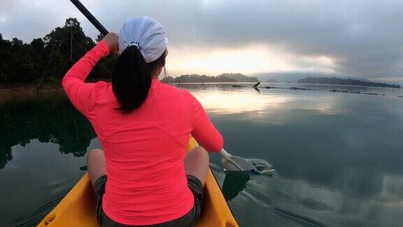 亚洲妇女皮划艇在早晨与阳光热带大湖放松的运动