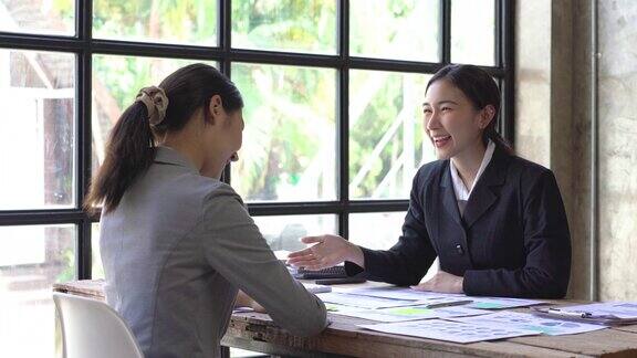 年轻的亚洲女性微笑着向女性合伙人客户握手表示同意感谢帮助在现代办公室建立合作关系