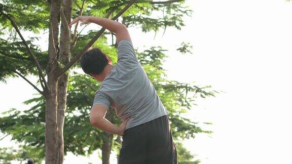 年轻的亚洲男子在户外运动前伸展身体热身周围是树木和夕阳的背景人们在户外锻炼是为了健康和幸福锻炼