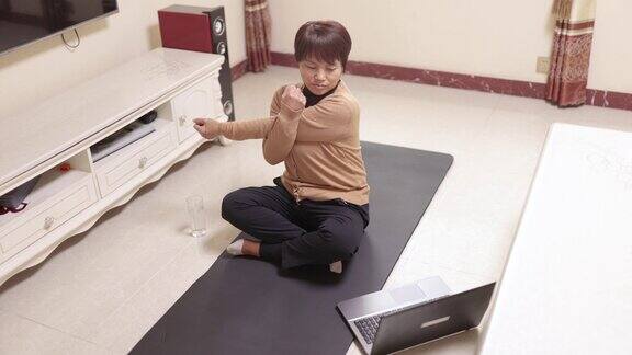 一位中年妇女用笔记本电脑在瑜伽垫上连接瑜伽科技和生活健康的生活方式