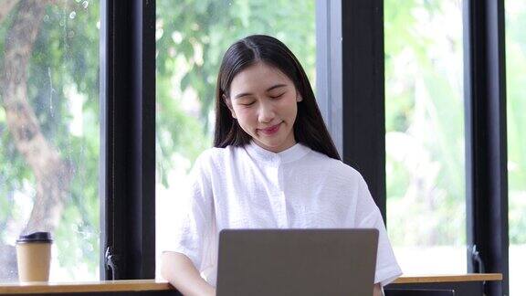 快乐的亚洲女性在笔记本电脑上工作在舒适的家里喝咖啡
