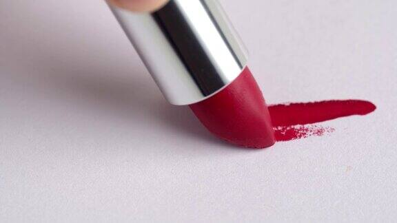 一个女人的手用红色的口红在白色的背景上做了一个记号化妆品唇彩唇膏涂抹涂抹描边在白色背景上涂抹唇彩化妆品的广告