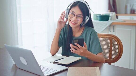 放松年轻的亚洲女性戴无线耳机在智能手机和笔记本电脑上听音乐女性喜欢听凉爽的音乐音频声音在家感觉没有压力