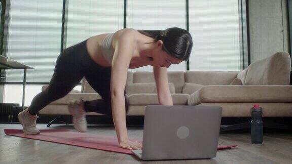 运动的亚洲妇女在运动服工作在家健身女在打开的笔记本电脑前摇着瑜伽垫重复着专业健身教练观看在线视频教程的指导