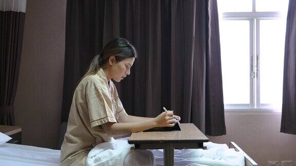 年轻的亚洲妇女在医院病床上看着窗外工作