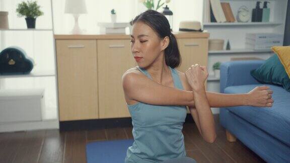 年轻迷人的亚洲运动女强人穿着运动服带着平静的感觉热身伸展练习瑜伽初学者在客厅的房子居家隔离锻炼和健身锻炼