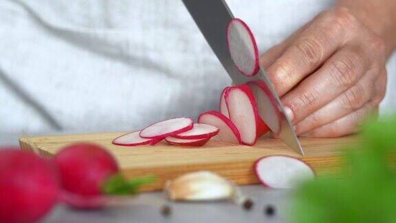 在厨房里在绿叶菜的背景上用手在木板上切萝卜切蔬菜烹饪食物