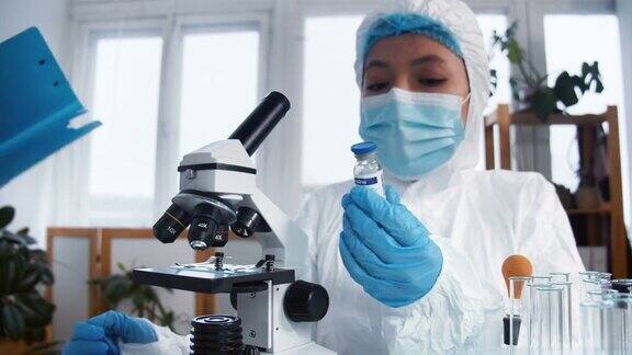 创建COVID-19疫苗两名女药学科学家穿着全套防护服在临床实验室测试新的治疗瓶