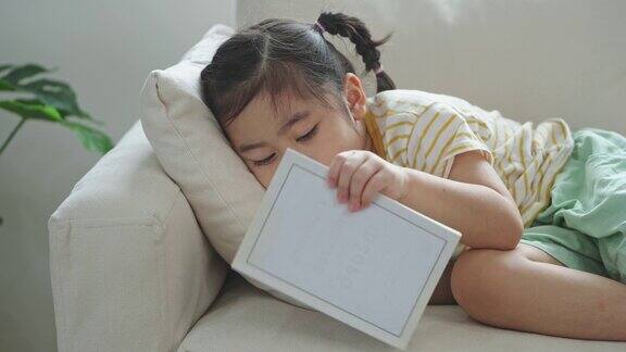 快乐快乐的亚洲儿童女婴微笑着坐在家里客厅的沙发上看书女孩放松地看书对着沙发微笑回到学校
