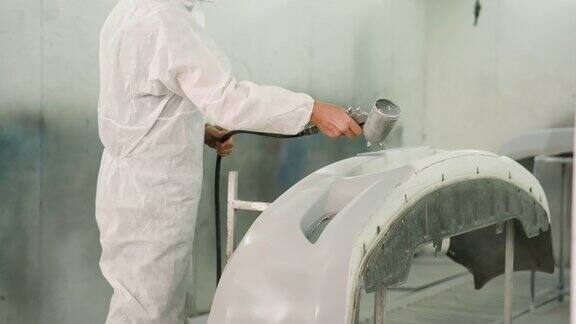 穿着白色PPE防护服的细心细致的白人工人在汽车保险杆上喷涂底漆送去修理汽车的油漆