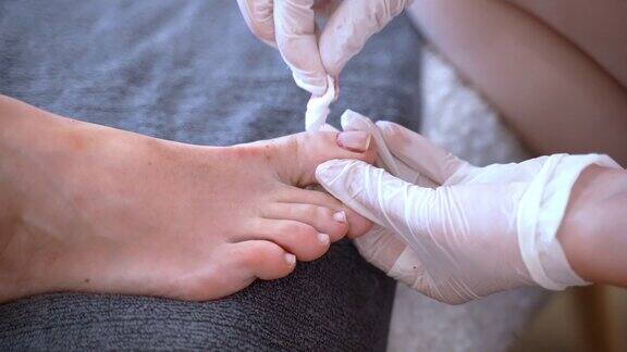 专业的美容师戴着一次性手套用丙酮溶液和化妆棉去除客户脚指甲上的旧指甲油足疗师准备女性的脚浸泡在温水中并进行进一步的足疗治疗脚趾甲程序纯度和