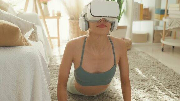 年轻的亚洲运动女性戴着虚拟现实头盔运动上衣和紧身裤在家里的客厅练习瑜伽饮食和健康减肥