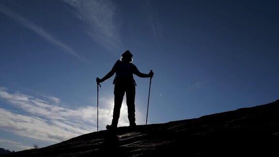日落时分拄着拐杖站在山坡上的徒步者的剪影