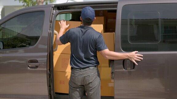 快递员从一辆货车上拿出盒子包裹然后去房子里把包裹送到房主那里