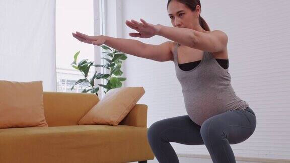 年轻漂亮的亚洲孕妇穿着运动服在家里做瑜伽