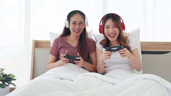 两姐妹戴着无线耳机在卧室的床上拿着操纵杆