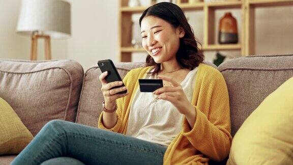 快乐电话或女孩网上购物与信用卡折扣或销售在数字金融科技网站在家里金融电子商务支付微笑或兴奋的亚洲女人坐在沙发上网上银行