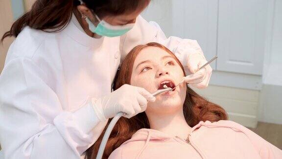 女牙医用斜面镜、吸唾液器等牙科设备为少女病人做牙科检查和牙齿清洁