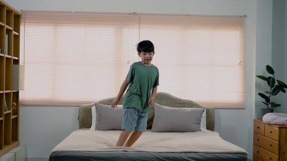 4K慢亚洲男孩英俊男孩穿着一件绿色的t恤他在床上跳上跳下一直跳一直跳不累他高兴地跳独自在卧室