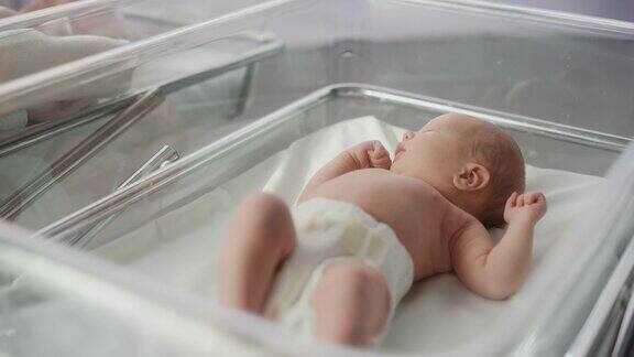 可爱的小婴儿躺在医院的小床上有趣的打哈欠白人婴儿花时间在妇产科诊所准备睡觉保健、怀孕和母亲概念