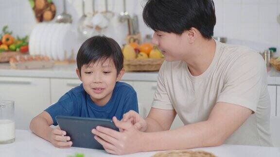 快乐的亚洲父亲和小可爱的男孩在家里聊天和使用平板电脑