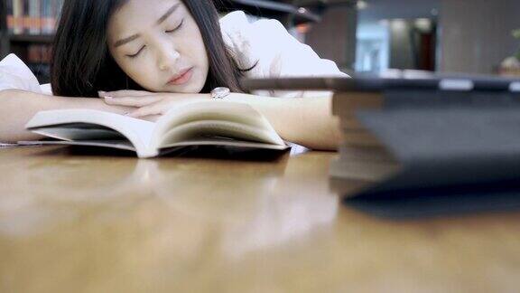 学生亚洲女孩午睡和睡觉在书桌上的书在图书馆教育