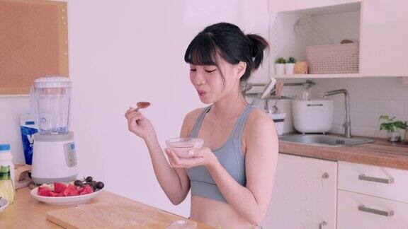 穿着运动服的亚洲女性享用美味的覆盆子酸奶心情愉悦又健康她喜欢在厨房里吃营养丰富的食物强调均衡饮食对她的健康有好处