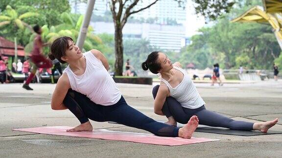 两个年轻的健身亚洲妇女练习瑜伽一起放松在城市公园