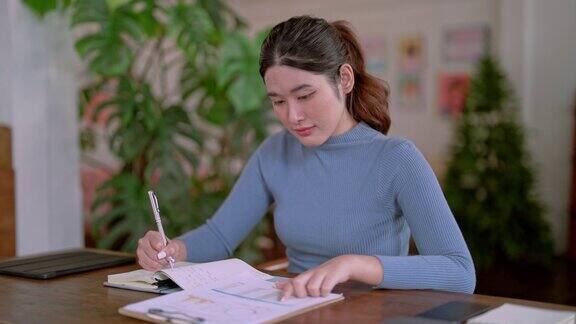 自信快乐的年轻亚洲女商人专注地坐在工作室里做笔记远程工作