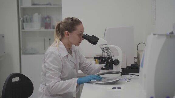 女性医学专业人员在显微镜后的医学实验室中进行样本分析工作女实验室技术员在医院通过显微镜分析样本医学微生物学