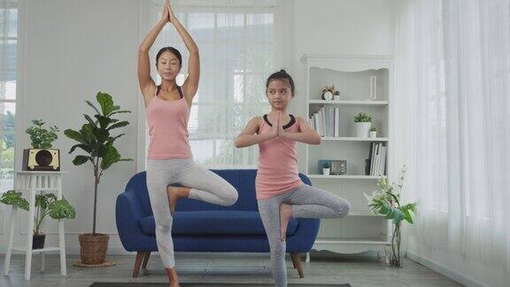 母亲和女儿正在家里练习瑜伽树式或菩提式